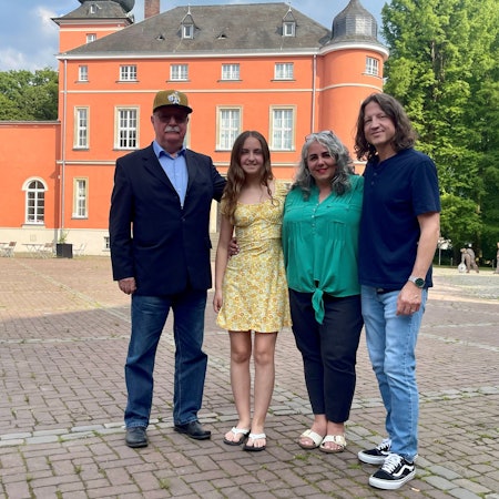 Zwei Männer und zwei Frauen stehen auf einem gepflasterten Hof.
