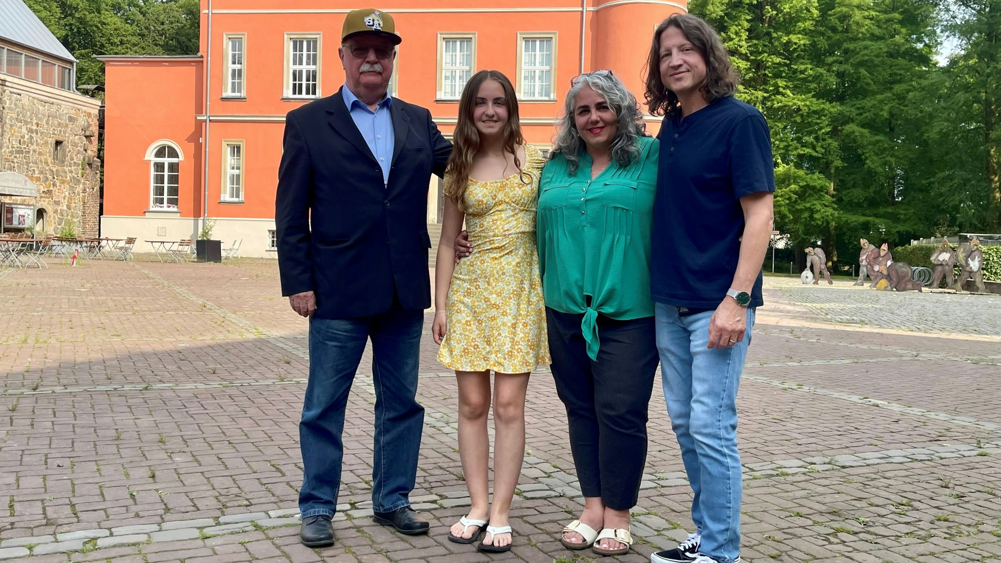 Zwei Männer und zwei Frauen stehen auf einem gepflasterten Hof.