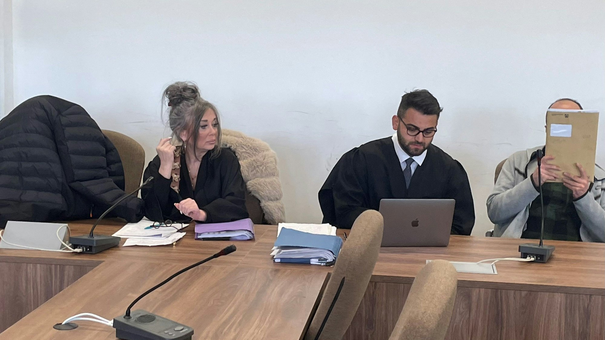 Die Angeklagte, dazwischen ihre Verteidiger, verstecken sich beim Prozessauftakt hinter einer Jacke und einer Mappe vor den Pressefotografen.