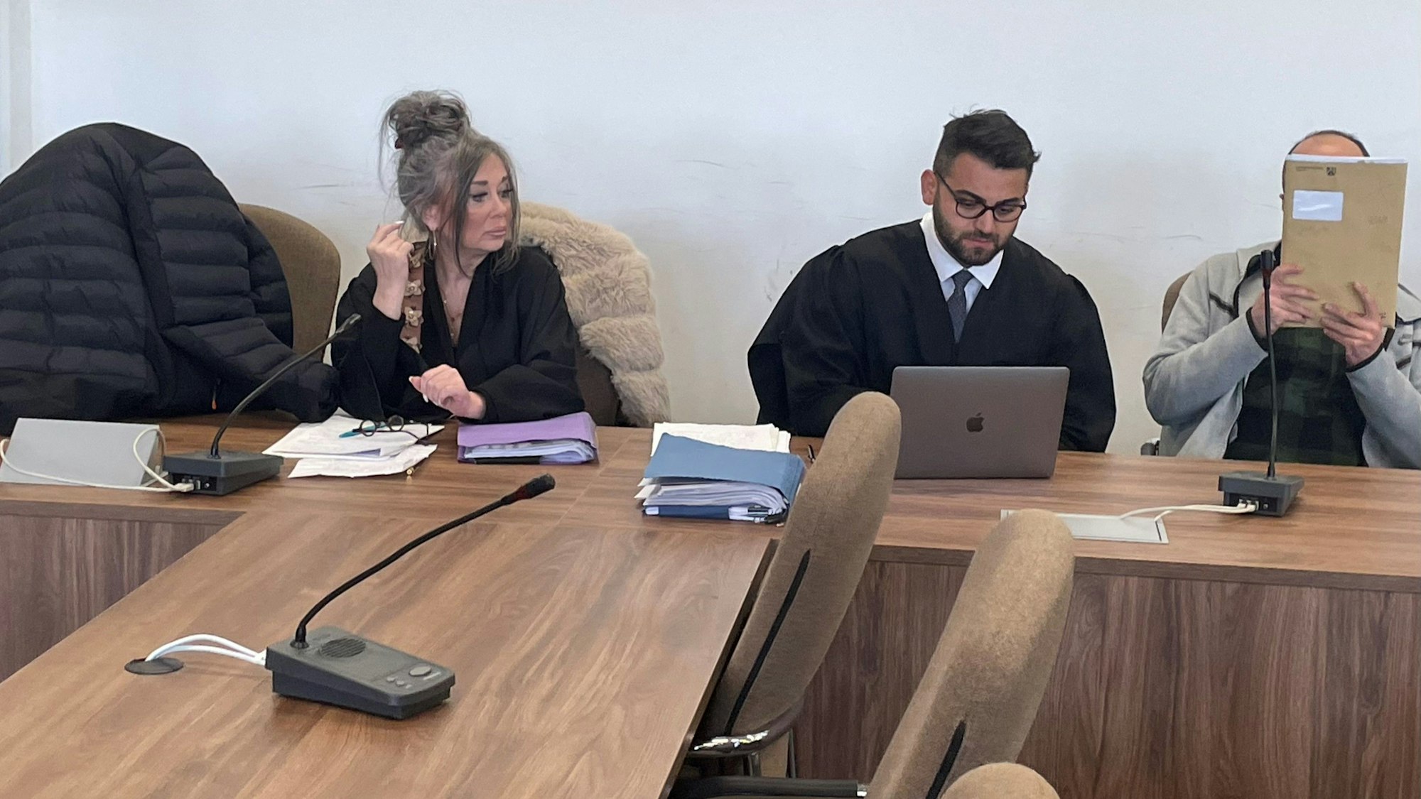 Die Angeklagten, dazwischen ihre Verteidiger, versteckten sich beim Prozessauftakt hinter einer Jacke und einer Mappe vor den Pressefotografen.