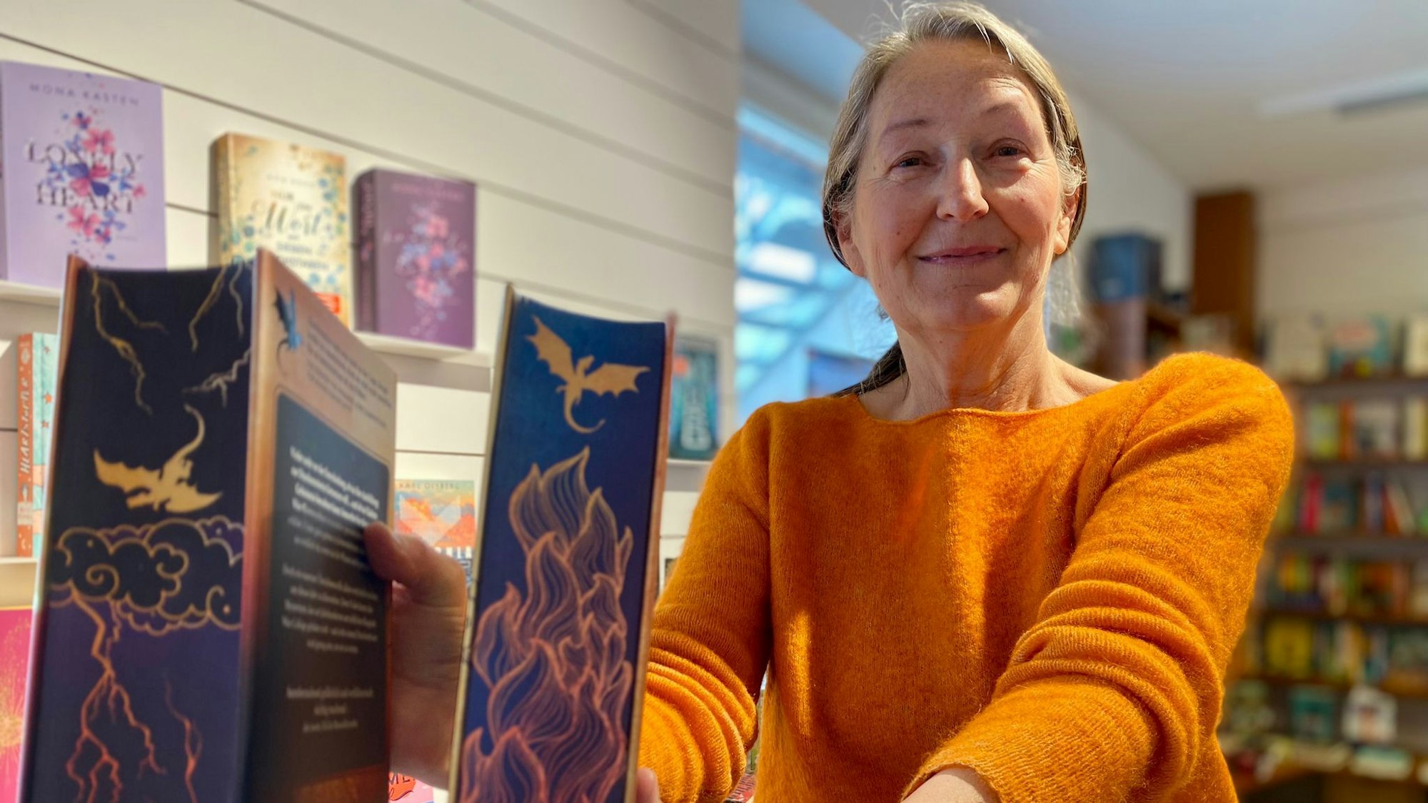 Katharina Pütz hält einen lilafarbenen Buchschnitt mit Drachen darauf in die Kamera.