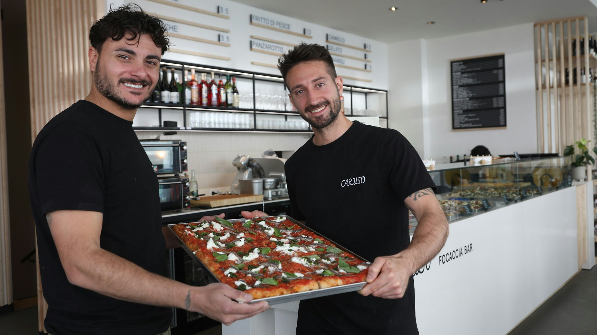 Betreiber der Caruso Focaccia Bar halten ein Blech mit Focaccia in die Kamera