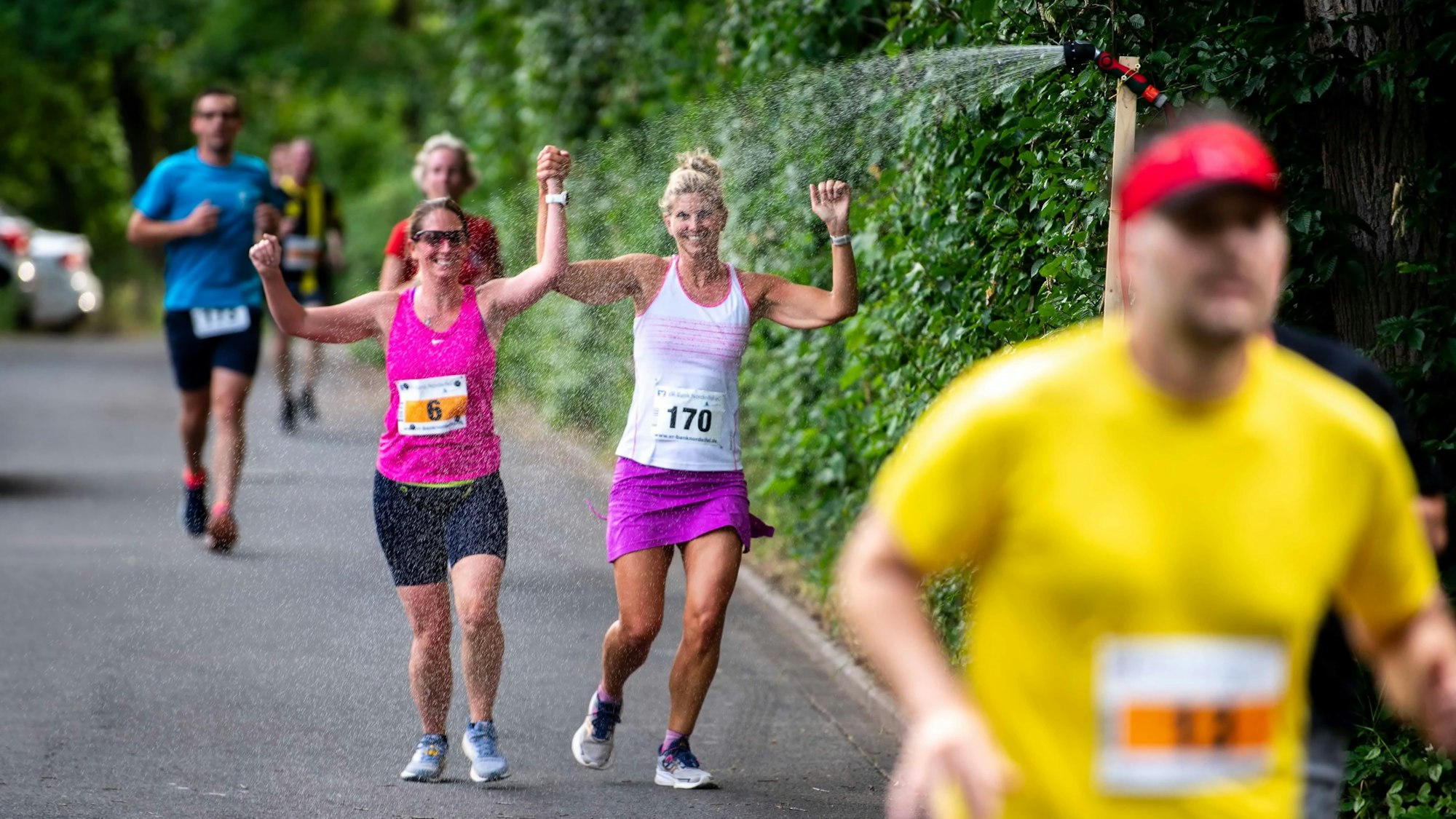Zwei Läuferinnen laufen durch den Strahl einer Freiluftdusche.