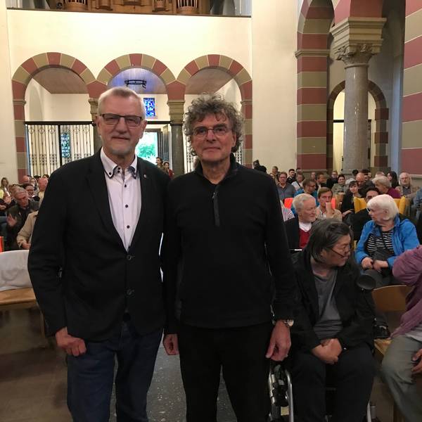 Zwei Männer vor einer Menschenmenge in einer Kirche