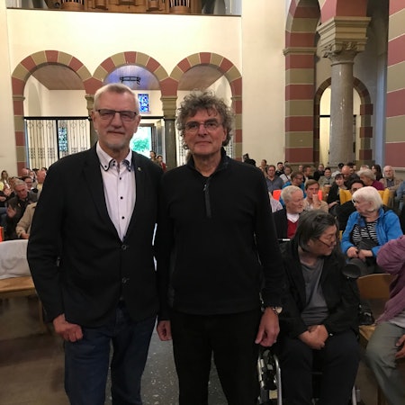 Zwei Männer vor einer Menschenmenge in einer Kirche