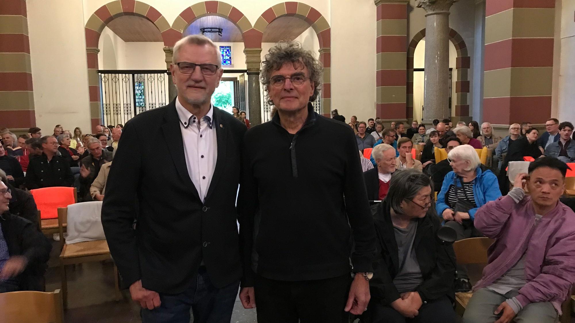 Zwei Männer vor einer Menschenmenge in einer Kirche