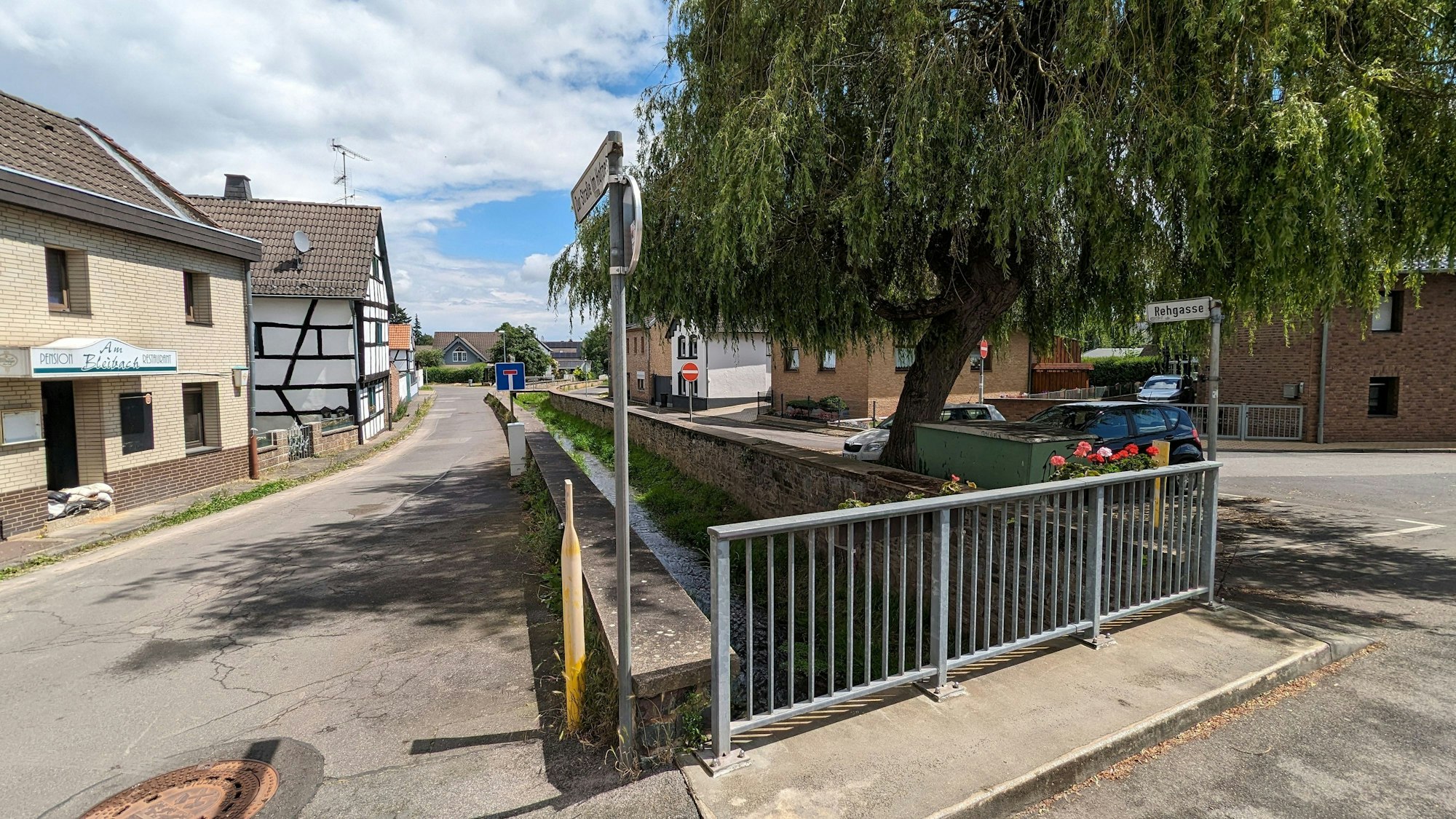 Im Bereich der Rehgasse in Kommern verläuft der Bleibach zwischen alten Ufermauern. Vorne ist das Geländer einer Brücke zu sehen.