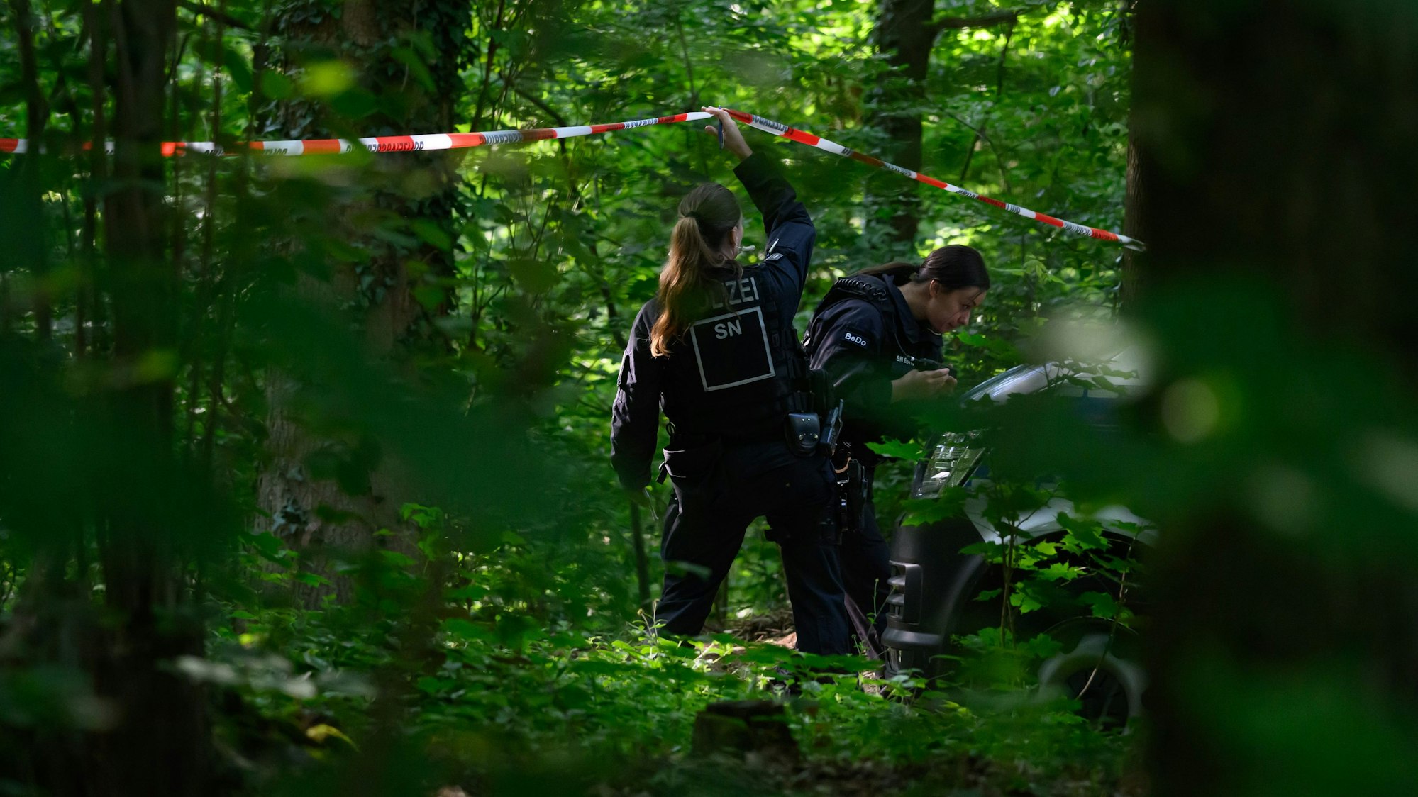 Eine Polizistin hebt ein Absperrband in einem Waldstück im sächsischen Döbeln nach oben. Dort hatte die Polizei bei der Suche nach der vermissten Valeriia eine Leiche entdeckt. Ob es sich dabei um das neunjährige Mädchen handelt, ist unklar.