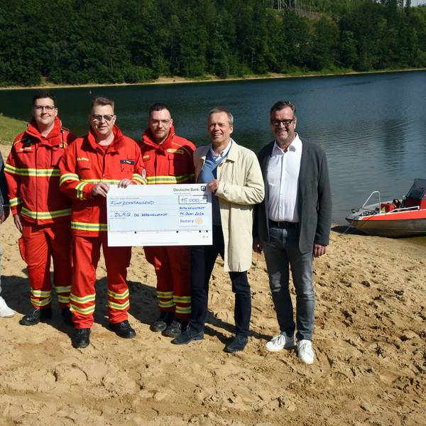 Spendenübergabe an der Aggertalsperre, mit Wasser und DLRG-Rettungsboot im Hintergrund.
