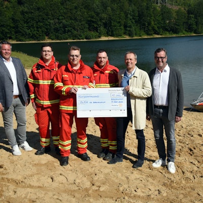 Spendenübergabe an der Aggertalsperre, mit Wasser und DLRG-Rettungsboot im Hintergrund.