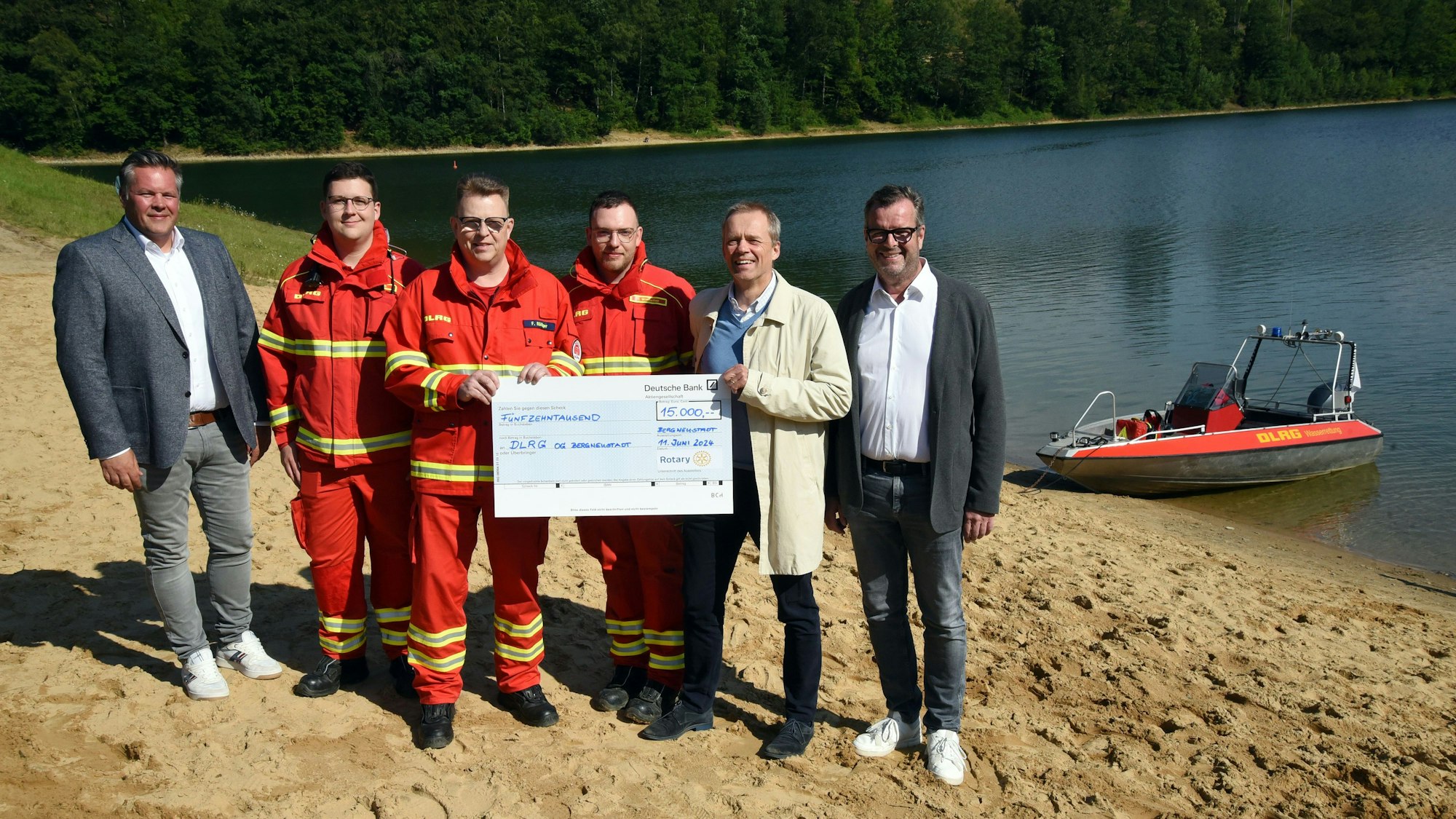 Spendenübergabe an der Aggertalsperre, mit Wasser und DLRG-Rettungsboot im Hintergrund.