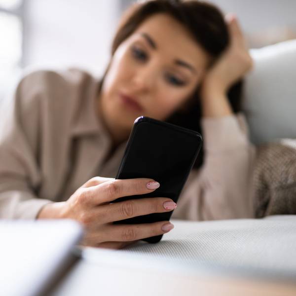 Eine Frau liegt auf dem Sofa und schaut auf ihr Handy.