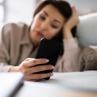 Eine Frau liegt auf dem Sofa und schaut auf ihr Handy.