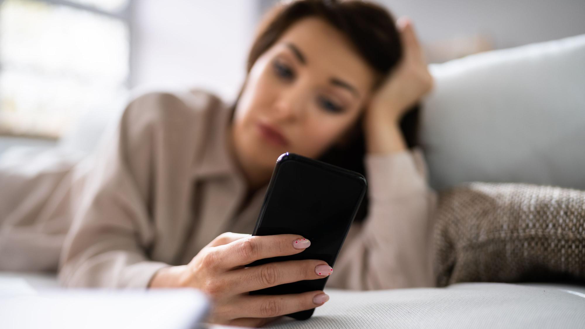 Eine Frau liegt auf dem Sofa und schaut auf ihr Handy.