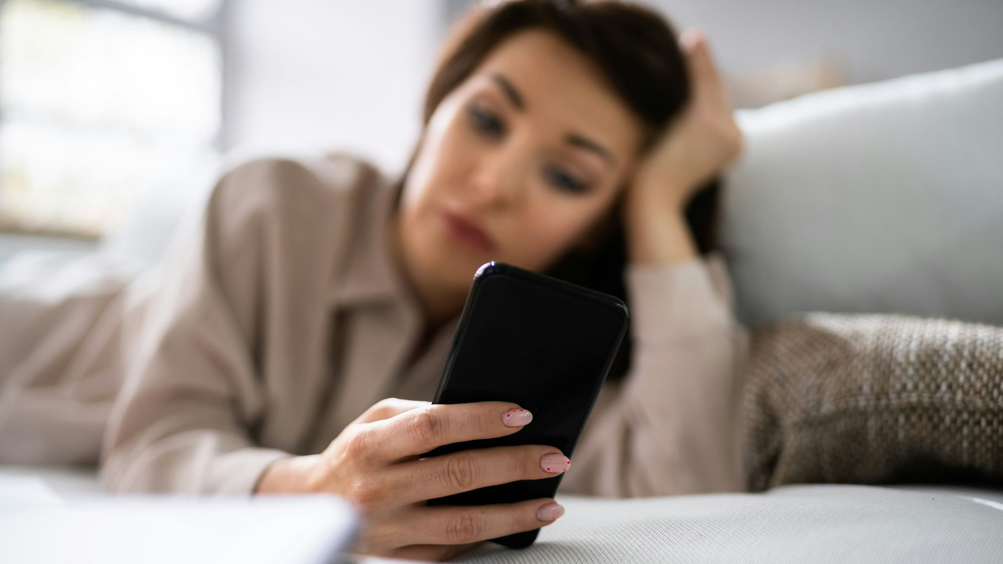 Eine Frau liegt auf dem Sofa und schaut auf ihr Handy.