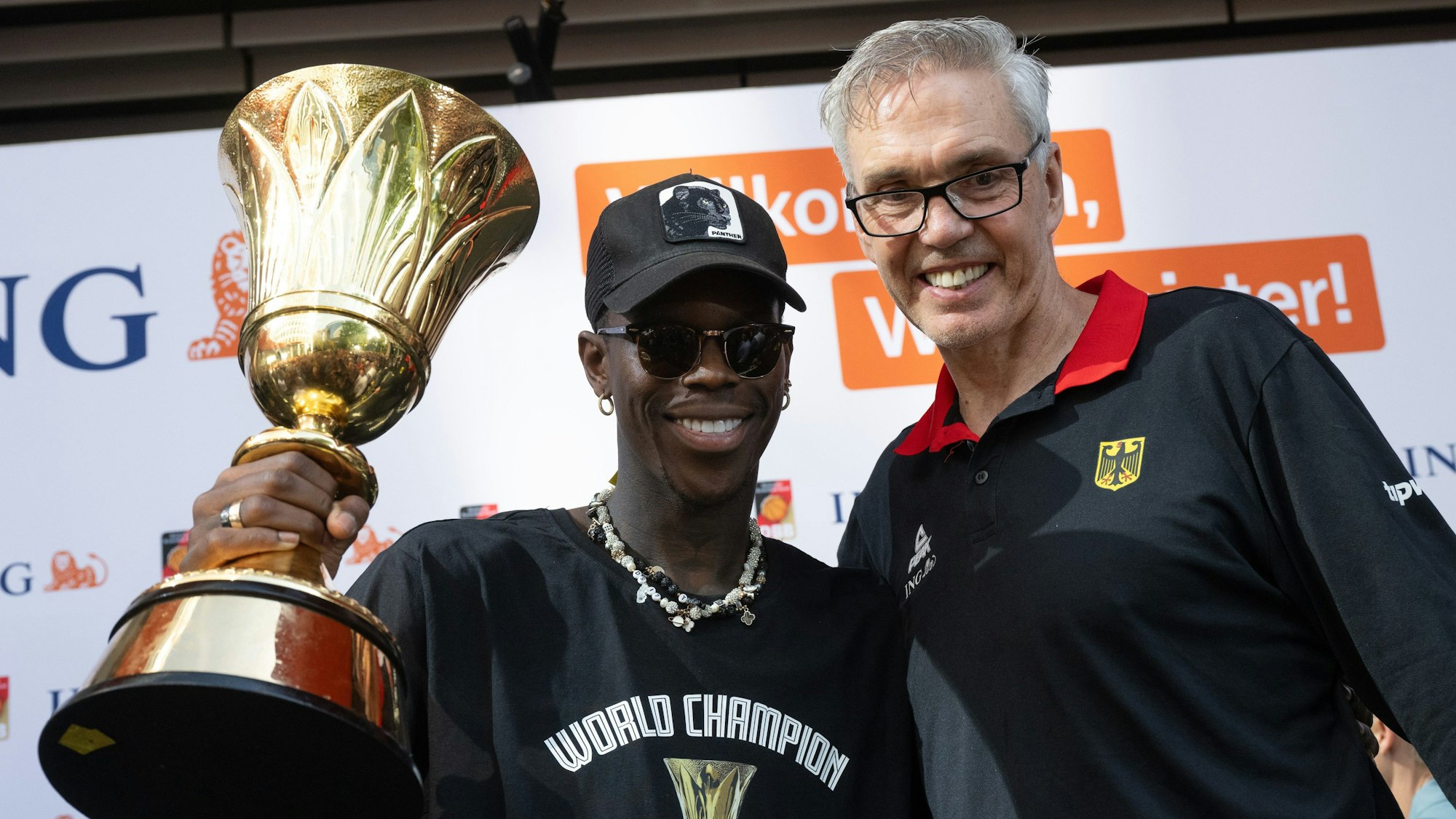 Dennis Schröder (l), Kapitän der Basketball-Nationalmannschaft, und Bundestrainer Gordon Herbert (r) jubeln beim Empfang des Teams in Frankfurt mit dem Pokal. Herbert verlässt die Nationalmannschaft nach Olympia.