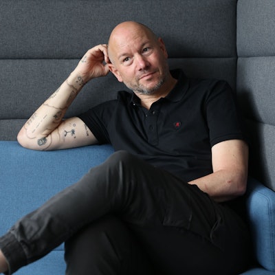 Porträtfoto von Mike Heßler, der auf einem Sofa sitzt.