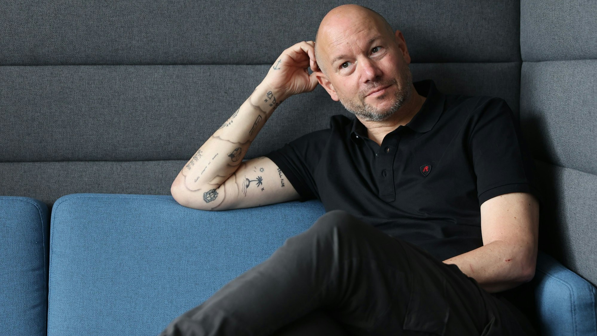 Porträtfoto von Mike Heßler, der auf einem Sofa sitzt.