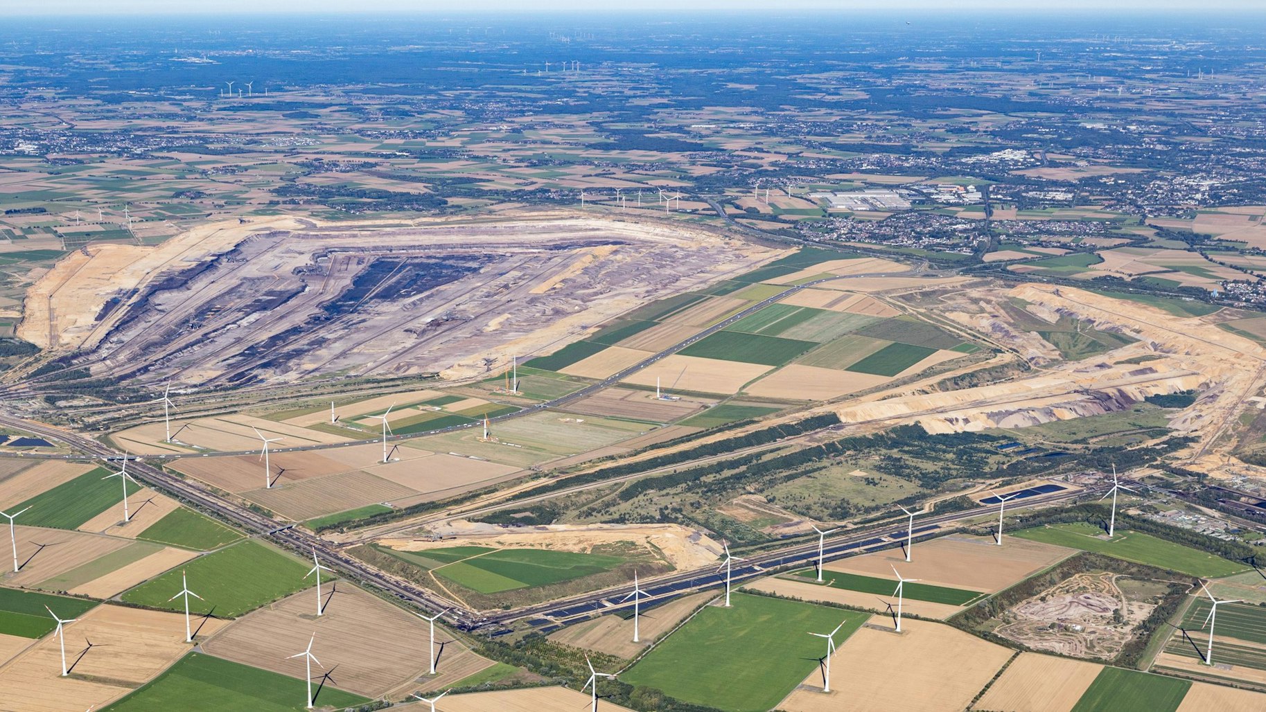 Der Tagebau aus der Vogelperspektive: Die riesige Abbaugrube ist zu sehen, drumrum Felder und Windräder, der Blick geht bis zum Horizont.