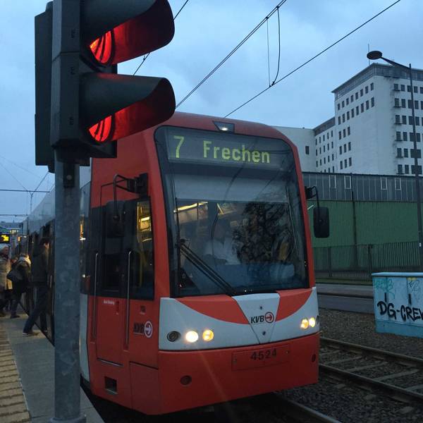Auf dem Foto ist eine rote Bahn der KVB zu sehen, die an einer Station hält.