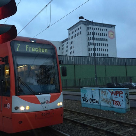 Auf dem Foto ist eine rote Bahn der KVB zu sehen, die an einer Station hält.