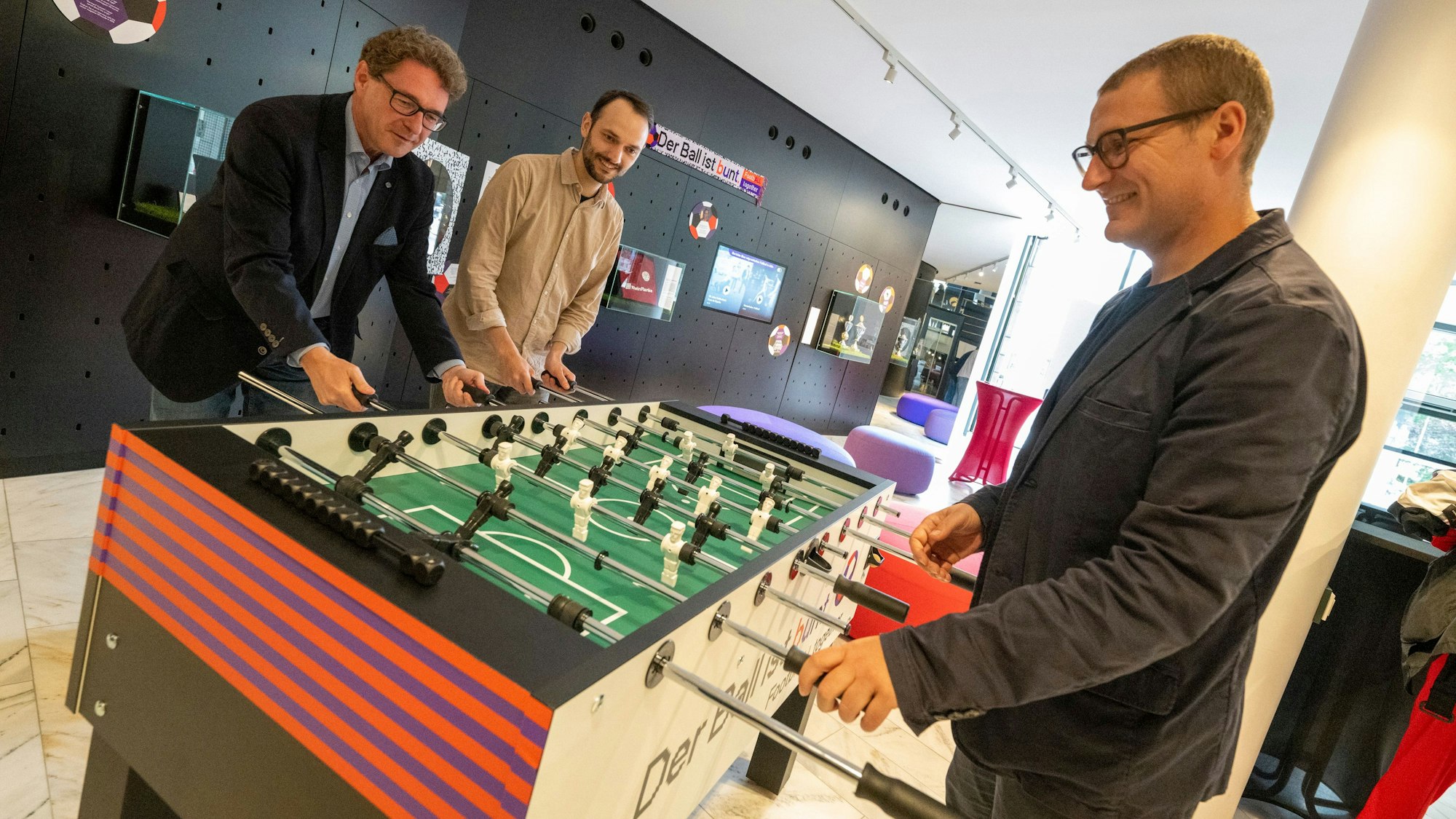 Drei Männer spielen Tischkicker.