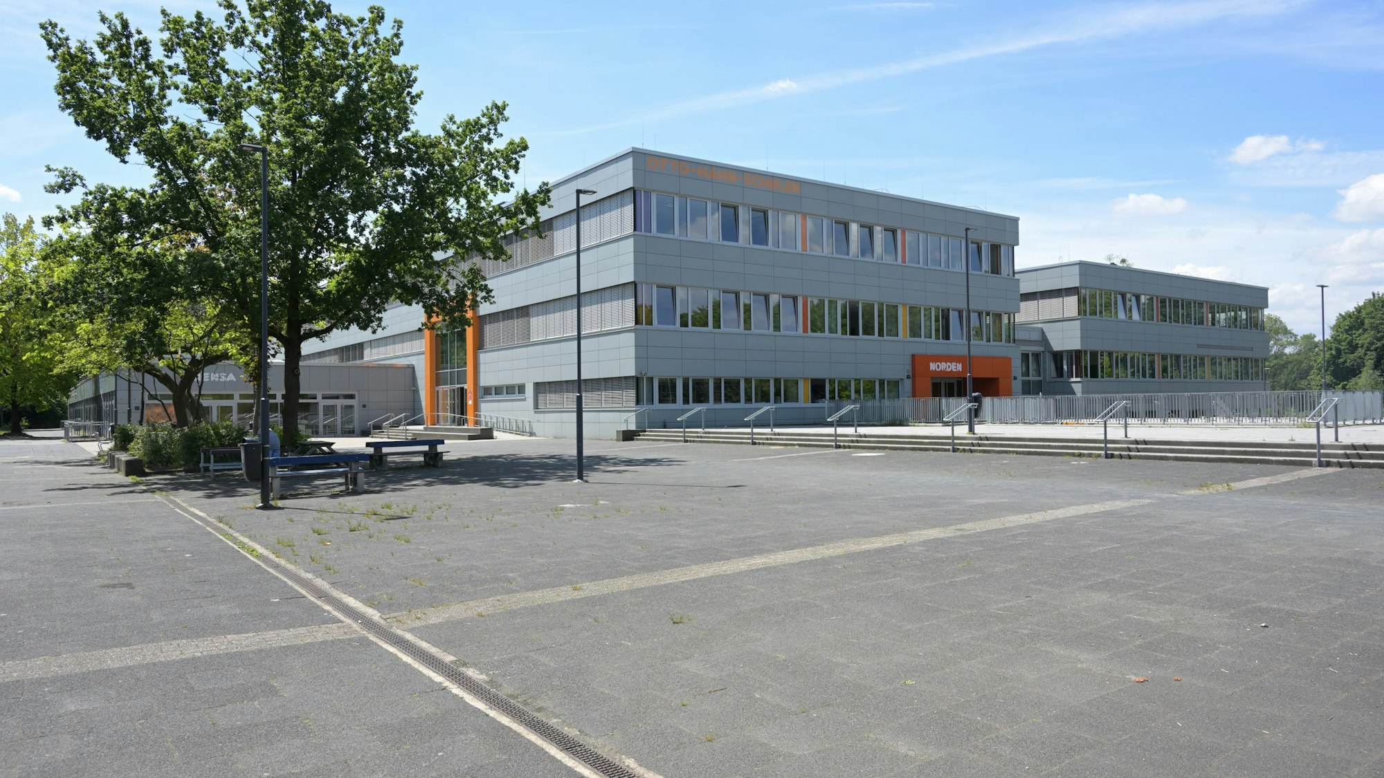 Außenansicht des dreistöckigen Schulzentrums, graue Fassade, orangefarbene Eingänge.