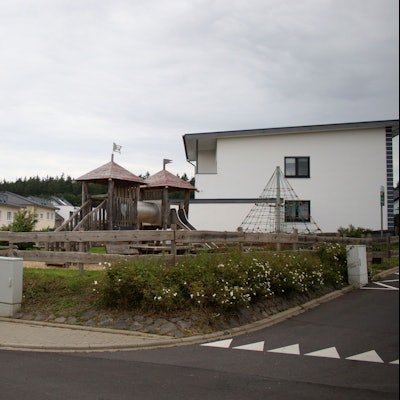 Das Bild zeigt den Spielplatz an der Stotzheimer Straße in Kirspenich von der Straße aus. Im Hintergrund die umliegenden Wohngebäude.