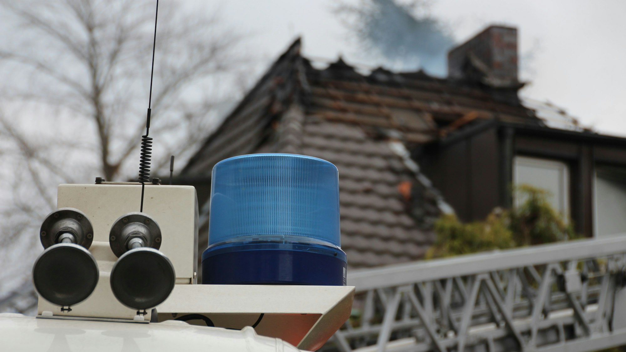 Ein Blaulicht ist vor einem Dachstuhl zu sehen, aus dem Rauch aufsteigt.