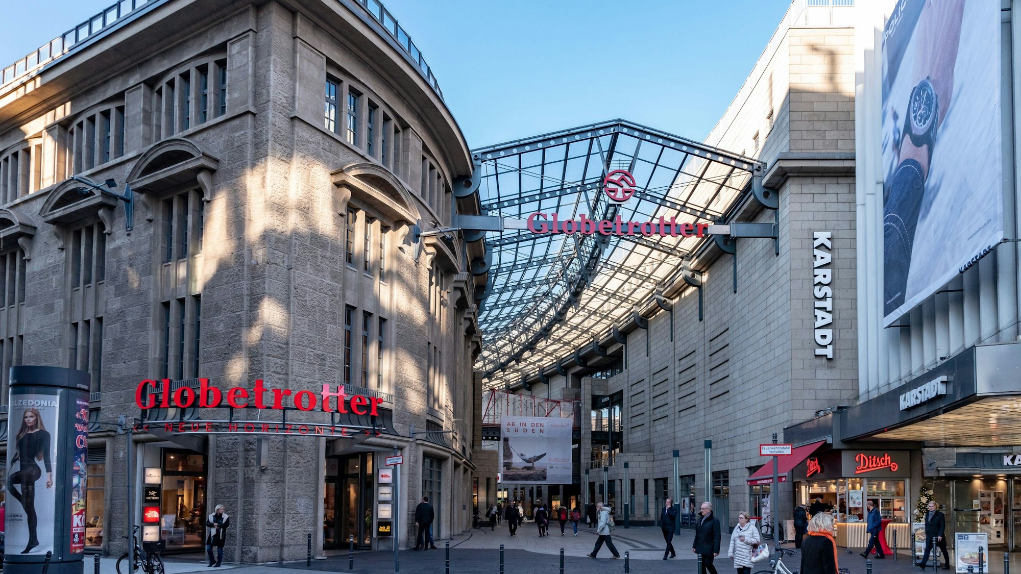 Zu sehen sind mehrere Geschäftshäuser in der Kölner Innenstadt, unter anderem die Schriftzüge „Globetrotter“ und „Karstadt“.