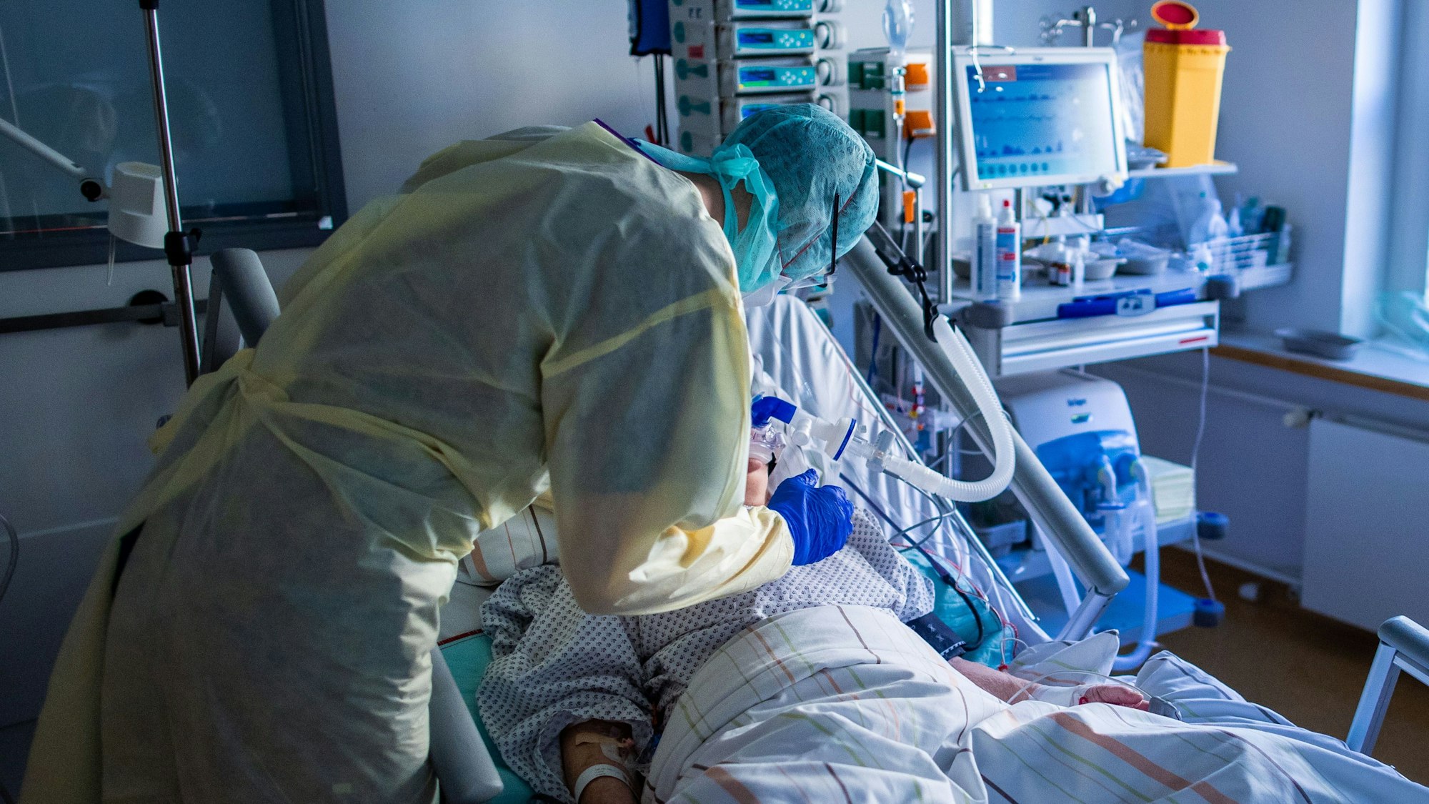 Ein Mitarbeiter richtet bei einer an Covid-19 erkrankten Patientin in einem Zimmer des besonders geschützten Teils der Intensivstation des Universitätsklinikums Greifswald die Beatmungsmaske.