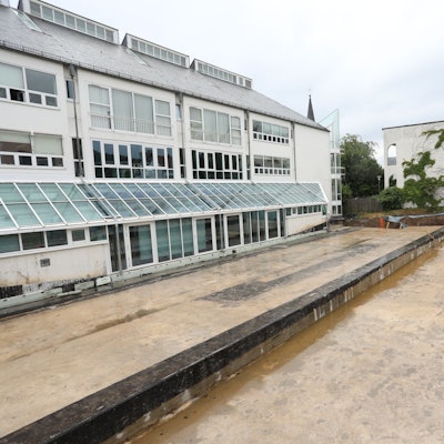 Eine rötliche Betonfläche auf der Rückseite eines Gebäudes, das mit vielen Fenstern versehen wurde.