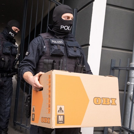 Ein Polizist trägt bei der Razzia gegen die mutmaßliche Schleuserbande im April 2024 einen Karton aus einem Gebäude.