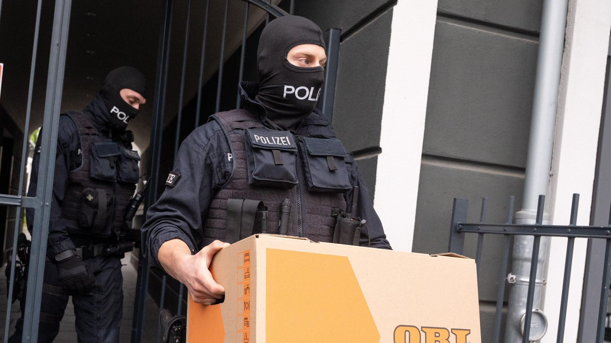 Ein Polizist trägt bei der Razzia gegen die mutmaßliche Schleuserbande im April 2024 einen Karton aus einem Gebäude.