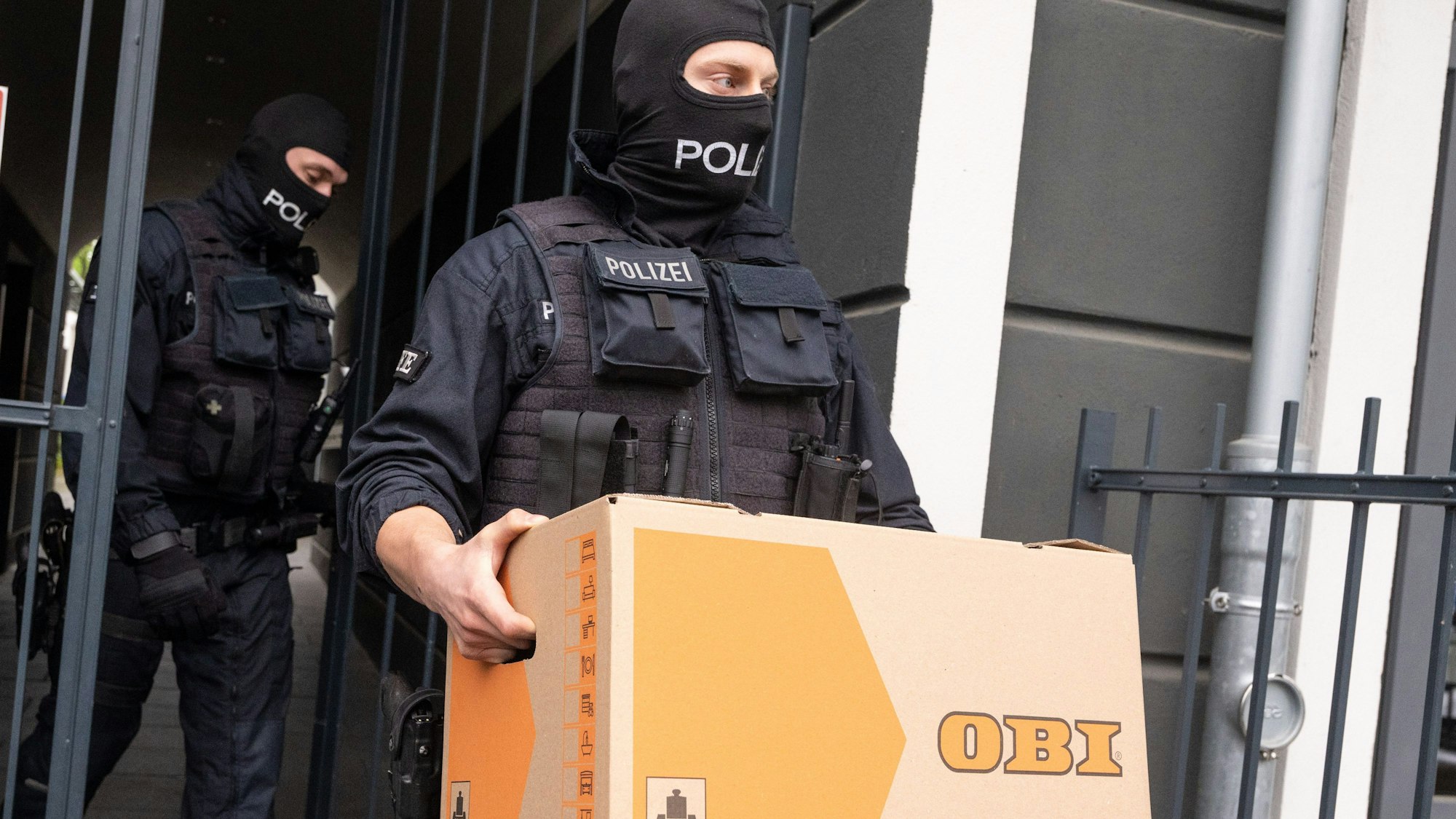 ARCHIV - 18.04.2024, Nordrhein-Westfalen, Bonn: Ein Polizist trägt im Rahmen einer Razzia gegen Schleuser einen Karton aus einem Gebäude.  (zu dpa: «Wüst zu Schleuser-Affäre: Spenden werden auf Anwaltskonten überwiesen») Foto: Benjamin Westhoff/dpa +++ dpa-Bildfunk +++