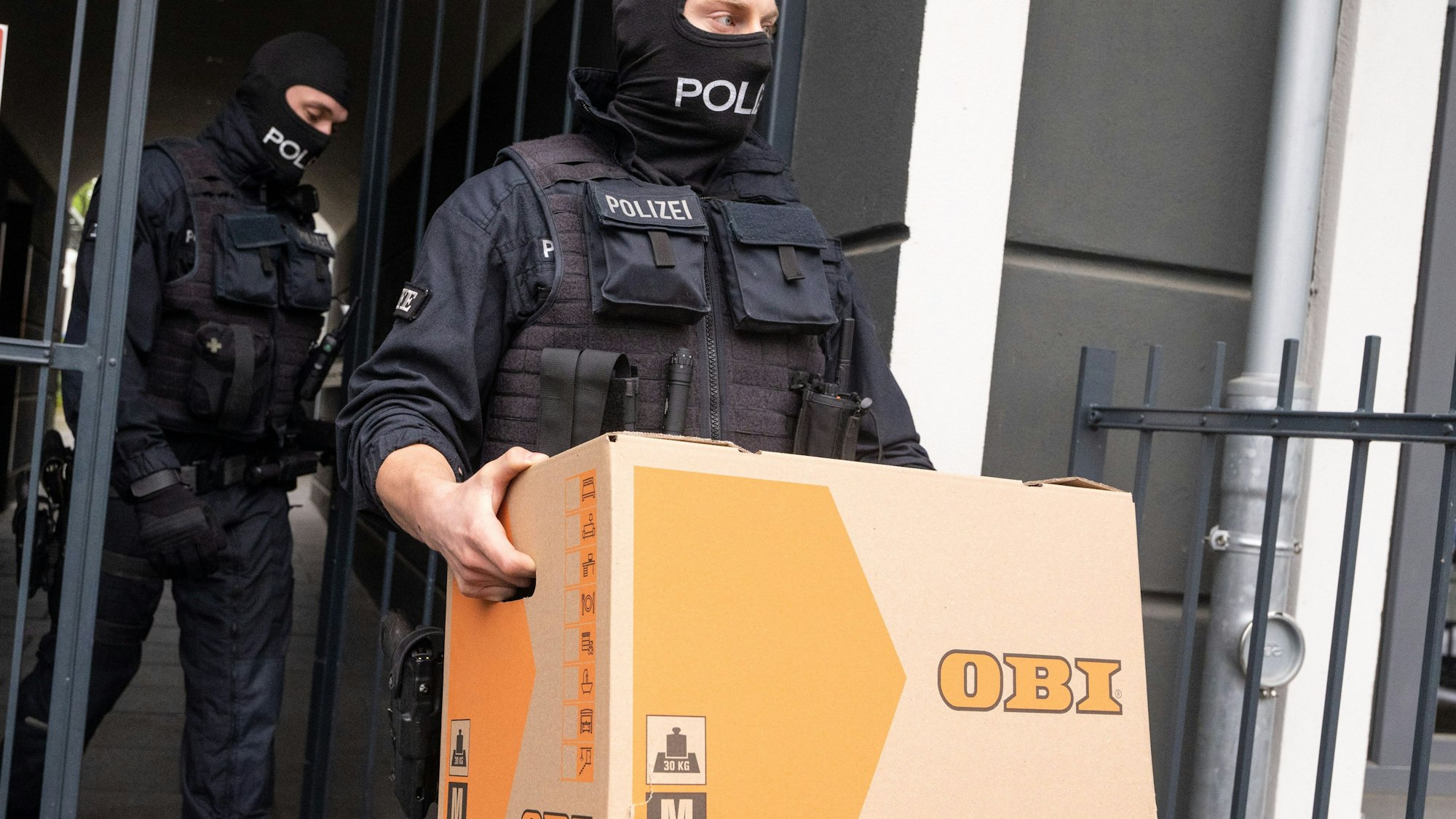 Ein Polizist trägt in Bonn bei der Razzia gegen die Schleuser einen Karton aus einem Gebäude.