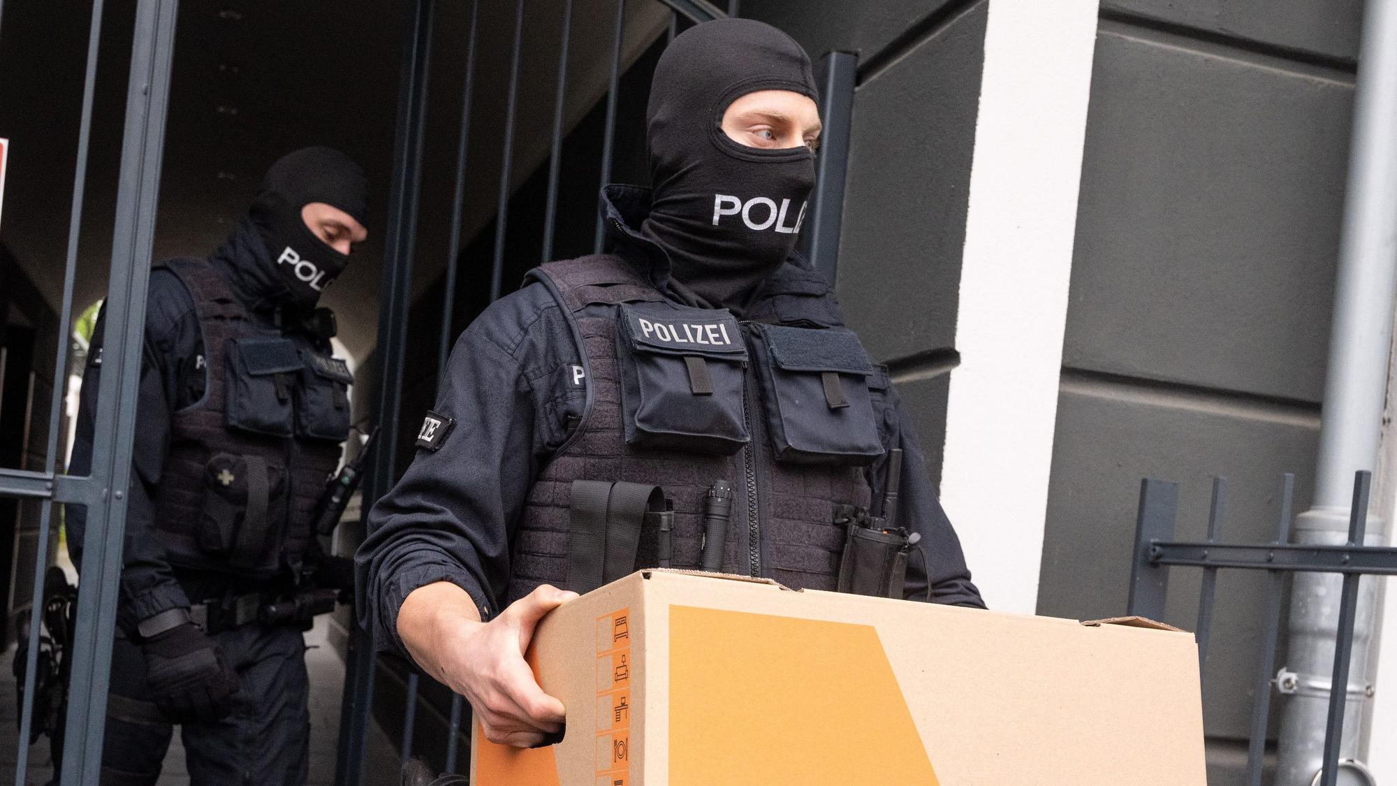 Das Bild zeigt zwei Polizeibeamte, die Kisten mit Beweismaterial tragen.