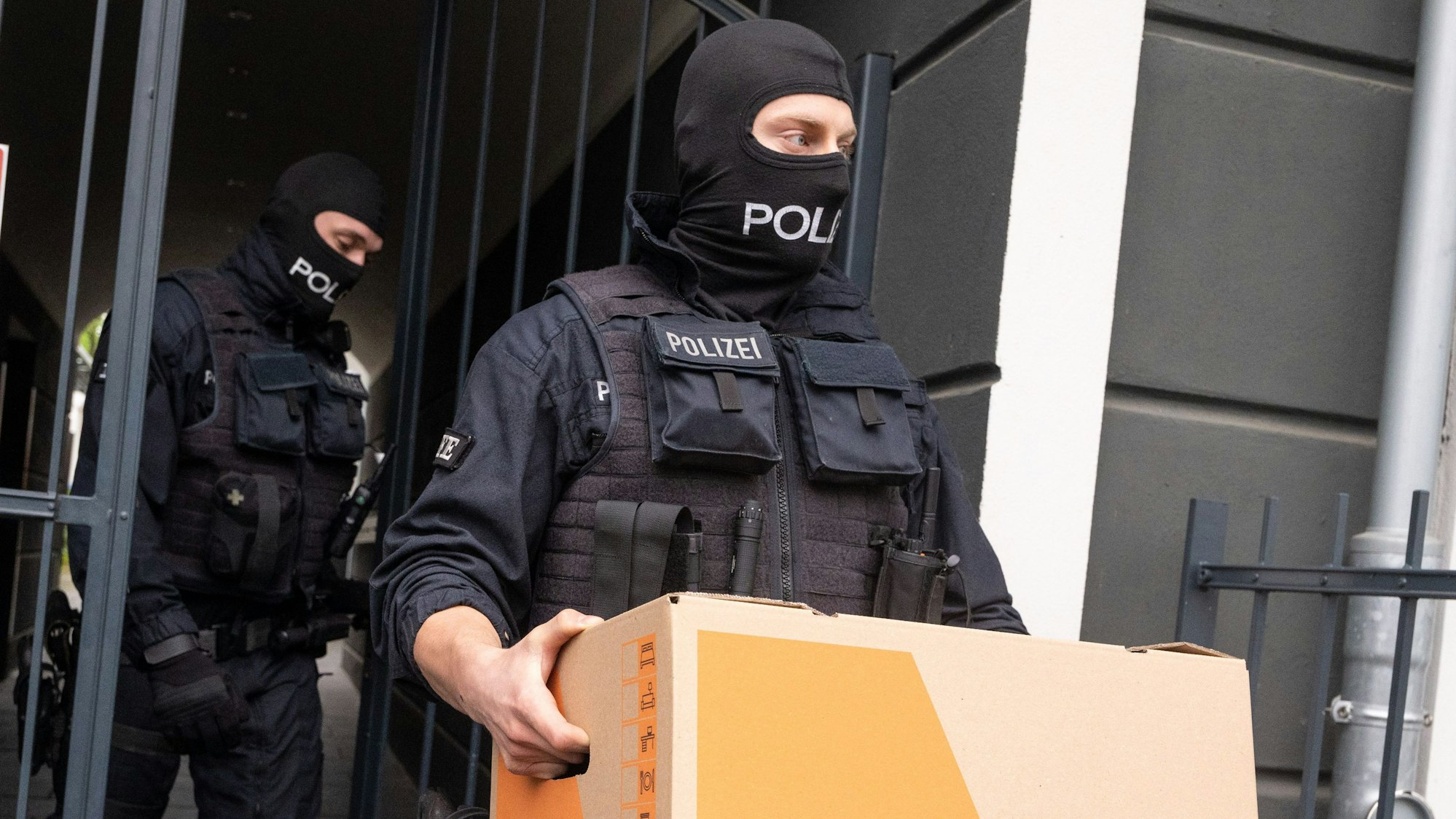Das Bild zeigt zwei Polizeibeamte, die Kisten mit Beweismaterial tragen.