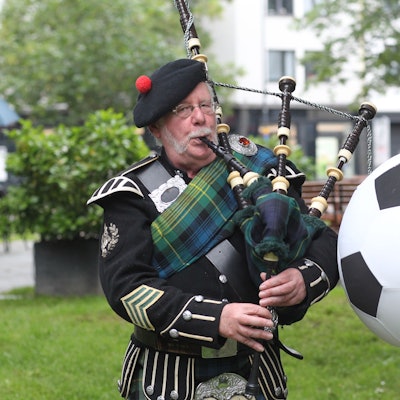 Peter Mac Coogan (65) mit Dudelsack und schottischer Tracht neben einen großen Fußball.