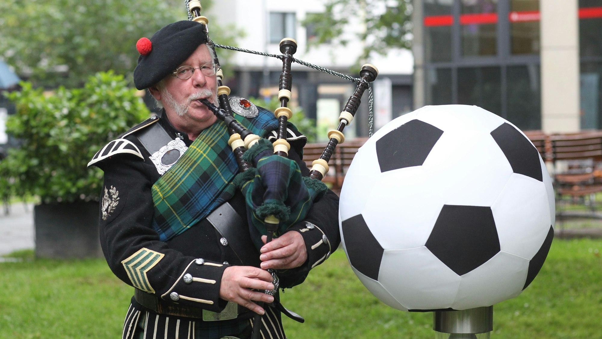 Peter Mac Coogan (65) mit Dudelsack und schottischer Tracht neben einen großen Fußball.