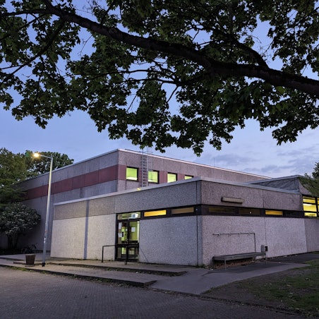 Ein beleuchteter Turnhallenkomplex bei Abenddämmerung.