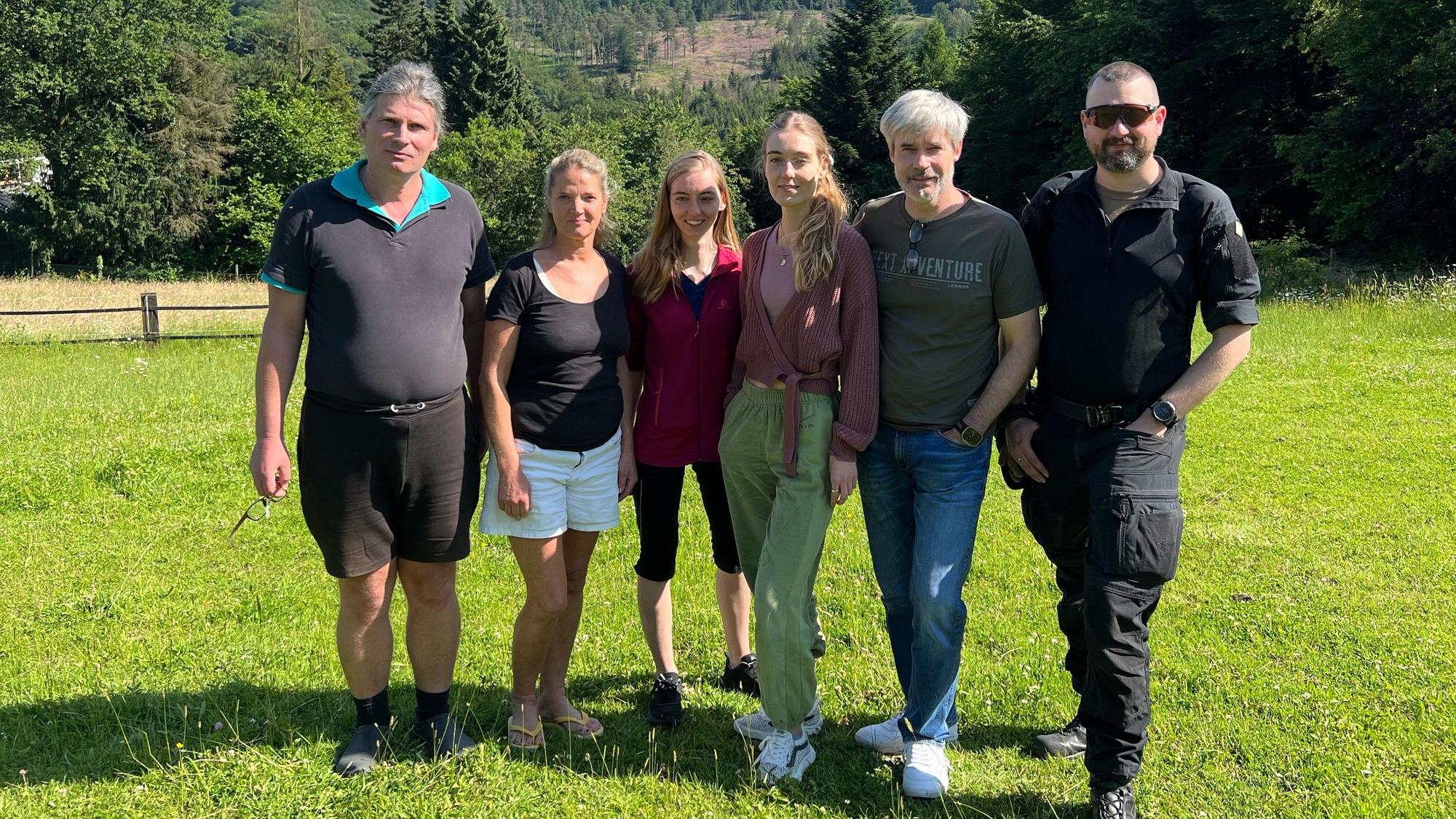 Drei Männer und drei Frauen stehen auf einer Wiese.