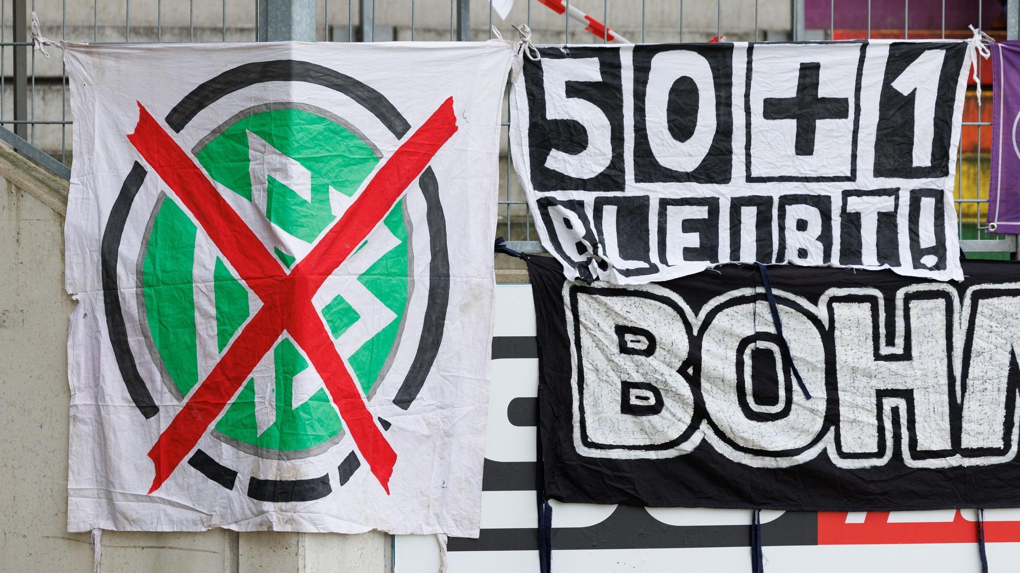 Ein Transparent mit einem durchgestrichenen DFB-Emblem und eines mit «50+1 bleibt!» ist am Zaun einer Tribüne zu sehen.