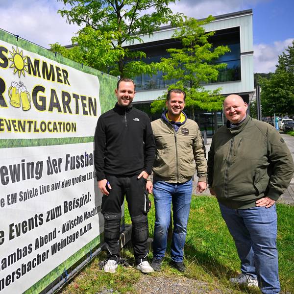 Timo Bay, Frank Hewel und Mike Bierögel stehen vor einem großen Banner, das auch den Sommer Biergarten mit Public-Viewing aller EM-Spiele hinweist.