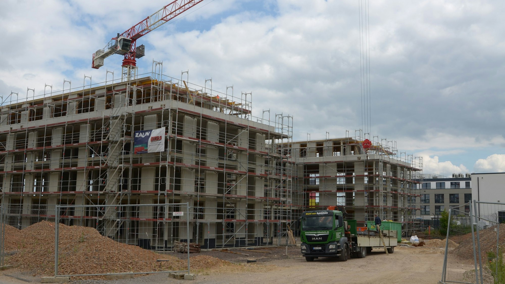 Vor dem Rohbau, der eingerüstet ist, steht ein Lastwagen. Im Hintergrund ist ein Baukran zu sehen.