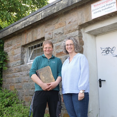 In Waldbröl-Hermesdorf wird der Wasserbeschaffungsverein 125 Jahre alt. Andrea Engelbert und Jürgen Greb stehen an einem Pumpenhaus. Greb hütet dessen altes Protokollbuch wie einen Schatz. Die beiden stehen vor dem Pumpenhäuschen in Hermesdorf.