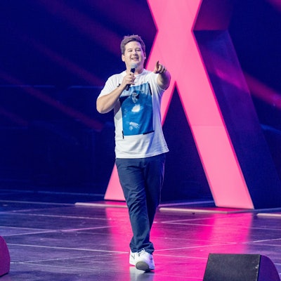 Chris Tall läuft über eine Bühne und zeigt in die Kamera.