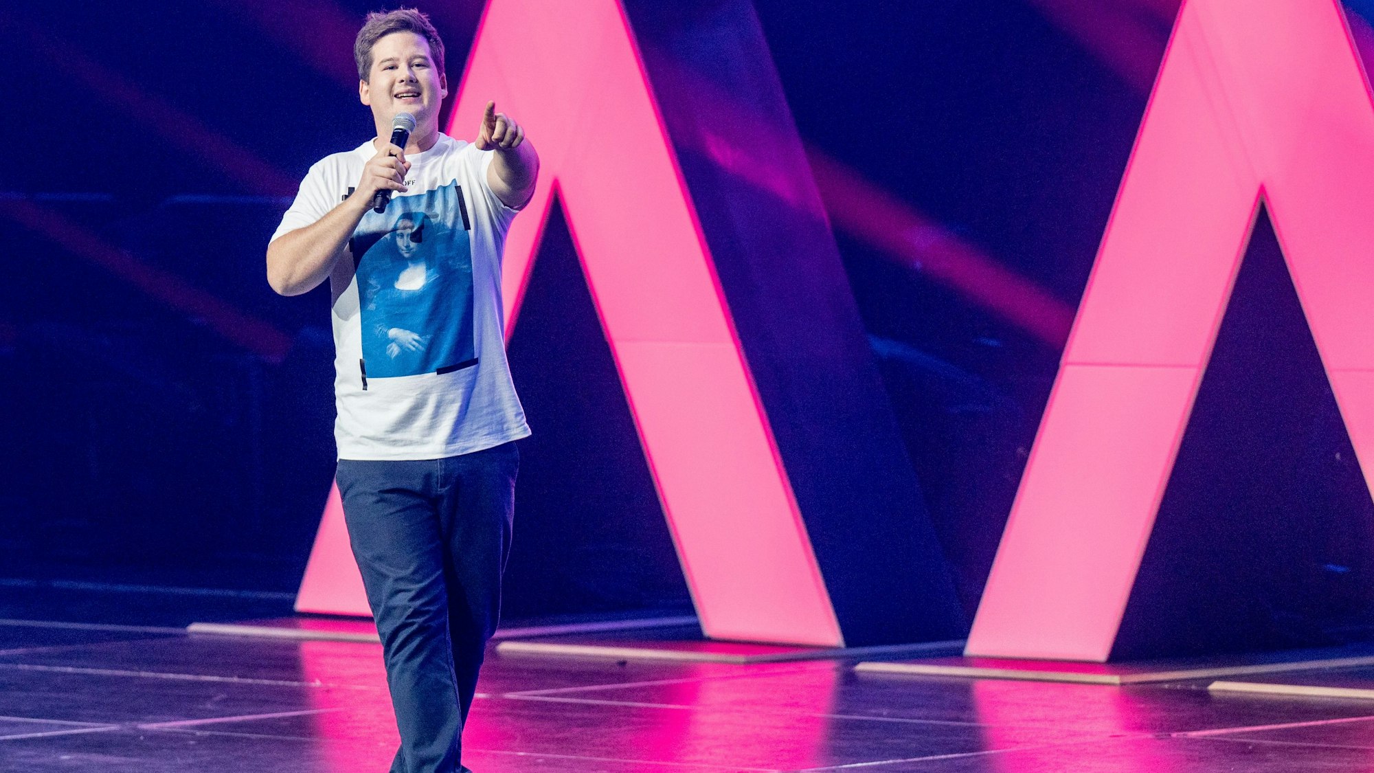 Chris Tall läuft über eine Bühne und zeigt in die Kamera.