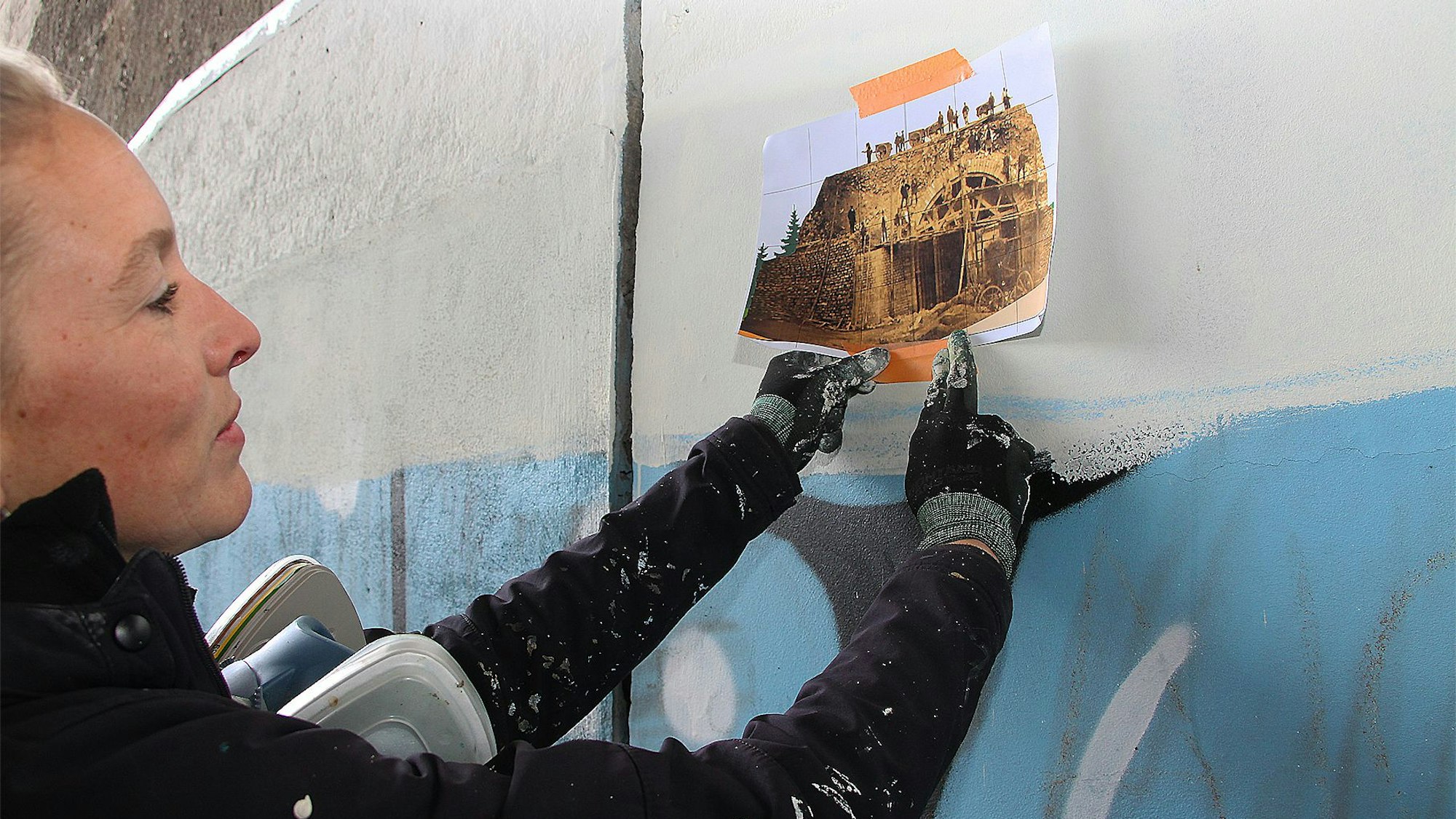 Lena Ortmann hält eine Kopie des alten Schwarz-Weiß-Fotos auf die Betonwand.