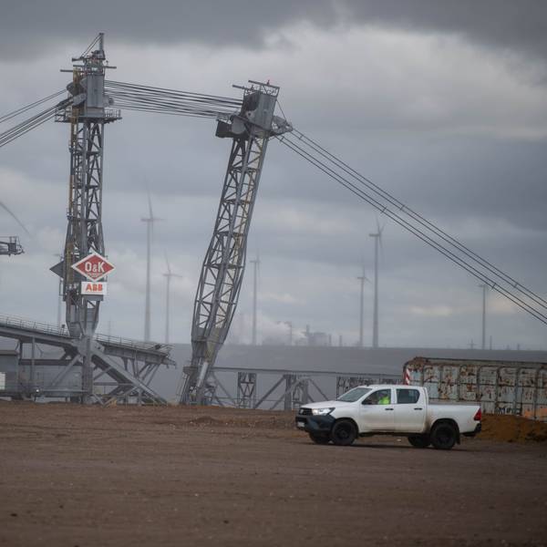 Das Bild zeigt einen Braunkohlebagger in der Nähe des ehemaligen Ortes Lützerath. Im Hintergrund sind Windräder zu erkennen.